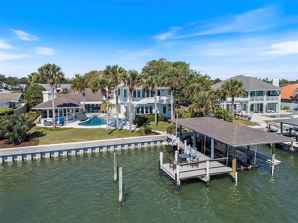 Wide aerial view of 1215 Commodore Drive in afternoon light, the two-story residence centered on its lawn with the salt-water pool, the covered dock, and the boat-lift bay extending into the Indian River