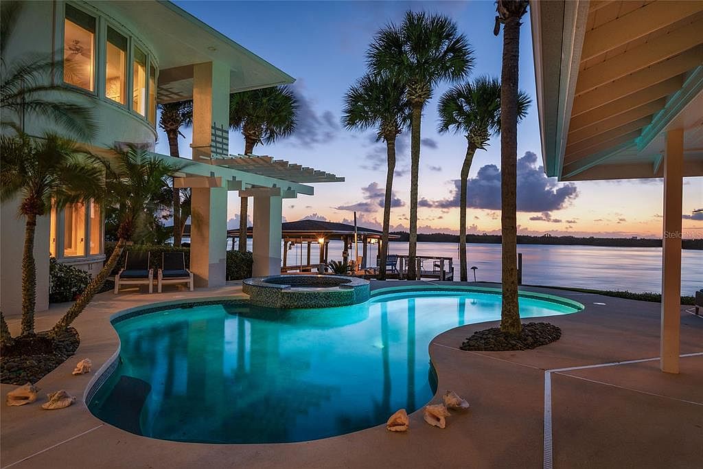 Salt-water pool and spa at 1215 Commodore Drive at twilight, with palm trees and the Indian River intracoastal stretching beyond, pink and orange sky on the eastern horizon